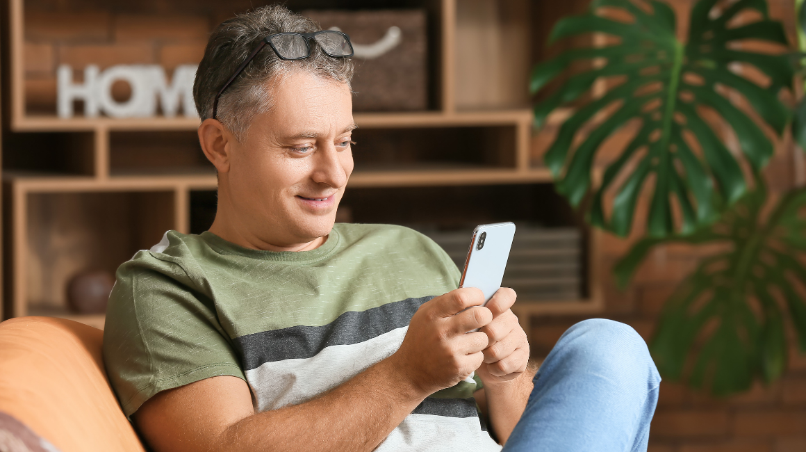 Zrelaksowany dojrzały mężczyzna korzystający ze smartfona w domowym zaciszu